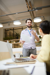 Wall Mural - Young office manager with paper standing in front of colleague and explaining her points of contract