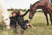 Two Young Beautiful Girls In Gear For Riding Near Their Horses. They Love Animals