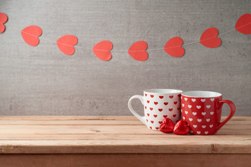 Wall Mural - Valentine's day background with coffee cups, heart shape chocolate and garland on wooden table