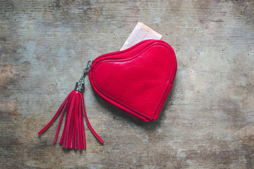 Top view of a red heart shaped leather wallet with money on wooden background. Shopping for Valentine's day, Birthday, engagement or wedding concept