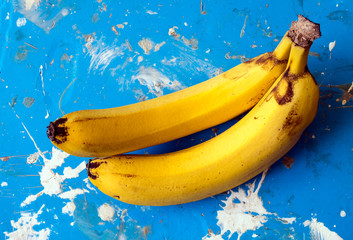 Two bananas on a blue background with spots and blots of white paint.