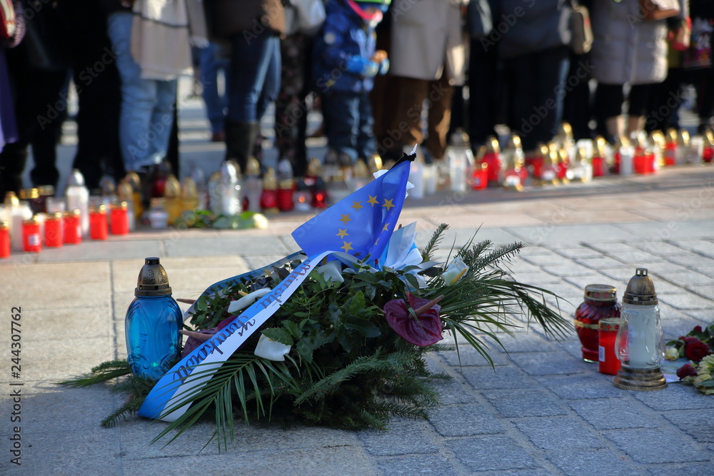 Wieniec kwiatów z flagą Unii Europejskiej i szarfą Rady Miasta Krakowa złożone na krakowskim Rynku po zamordowaniu prezydenta Gdańska Pawła Adamowicza, w tle rozmyte znicze, zgromadzeni ludzie - obrazy, fototapety, plakaty 
