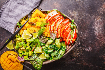 Wall Mural - Grilled chicken, mango and avocado salad in dark dish on dark background, top view.