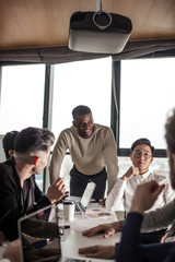 Wall Mural - mixed race business team listening to african american male speaker discussing presentation on flip chart at meeting in boardroom, corporate training concept, midsection shot with focus on speaker.