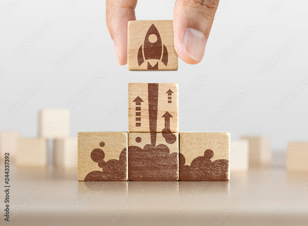 Business start up, start, new project or new idea concept. Wooden blocks with launching rocket graphic arranged in pyramid shape and a man is holding the top one. - obrazy, fototapety, plakaty 