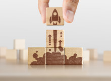 Business Start Up, Start, New Project Or New Idea Concept. Wooden Blocks With Launching Rocket Graphic Arranged In Pyramid Shape And A Man Is Holding The Top One.