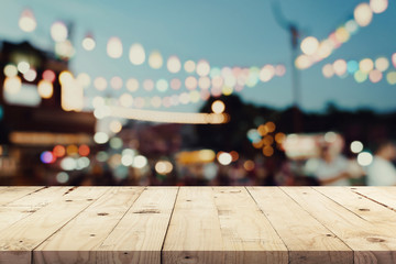 Wall Mural - Empty wooden table and blurred background at night market festival people walking on road with copy space, display montage for product.