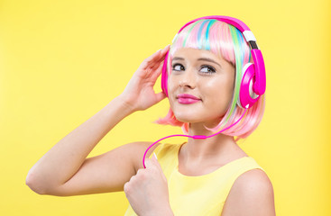 Woman in a colorful wig with headphones listening to music on a yellow background