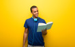 © luismolinero - African american man with blue t-shirt on yellow background holding a book and enjoying reading