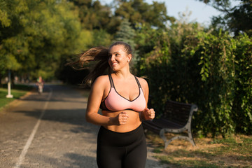 young beautiful smiling plus size woman in sporty top and leggings joyfully looking aside while runn
