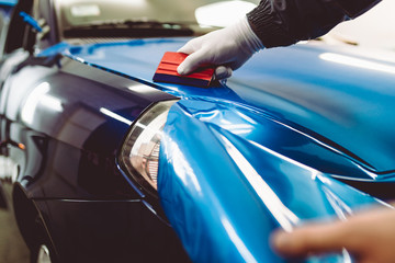 Car wrapping specialist putting vinyl foil or film on car. Selective focus.