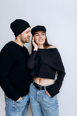 Wall Mural - Two hipster models: a man and a woman in a blank black t-shirt, jeans and posing. in a black hat, cap, love, kisses