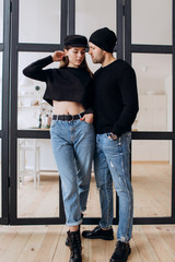 Wall Mural - Two hipster models: a man and a woman in a blank black t-shirt, jeans and posing. in a black hat, cap, love, kisses