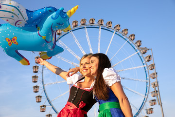 2 junge sexy Frauen haben Spass auf dem Frühlingsfest, Oktoberfest, Wiesn, mit Lebkuchenherz Schokobane vor dem Riesenrad Luftballons