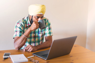 indian with turban working with his laptop and holding a cup of coffee