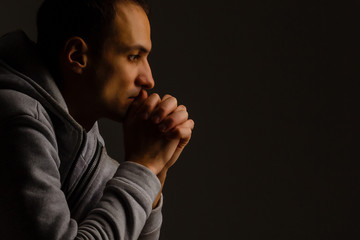 Poster - Religious young man praying to God on dark background, black and white effect