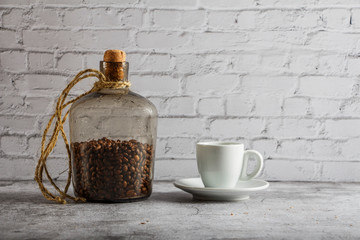 Wall Mural - White cup with black coffee and grains of coffee in a bottle on a background of gray stone. Place for text. Mock up vintage concept.