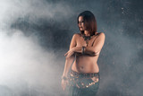 Sexy women performs belly dance in ethnic dress on dark smoky background