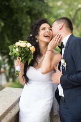 Wall Mural - Woman and man smile on wedding day. Groom kiss happy bride with bouquet. Wedding couple in love. Newlywed couple on summer outdoor. Marriage concept. love and family