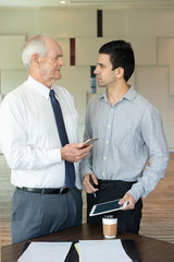 Wall Mural - Indignant businessmen looking at each other. Serious entrepreneur with smartphone in hand looking at his employee. Confrontation concept