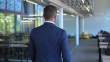 Back View Business Man Wearing Formal Blue Suit Walking In Open Space Office. Employee Walks In Mobern Lobby