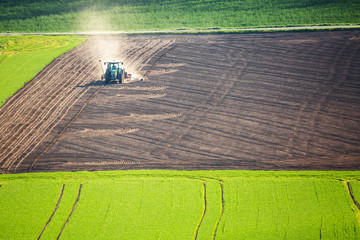 Beautiful spring landscape with working tractor on green and brown field in South Moravia, Czech Republic. Agriculture concept.