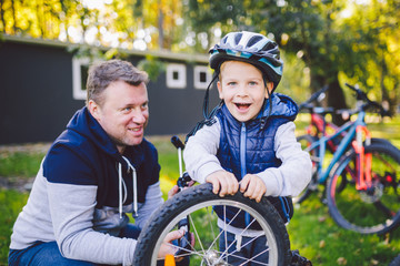 Father's day Caucasian dad and 5 year old son in the backyard near the house on the green grass on the lawn repairing a bicycle, pumping a bicycle wheel. Dad teaches how to repair a child's bike