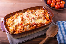 Baked fusilli pasta with mozzarella and tomato in a pan for baking on a wooden rustic background, top view.