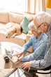 © Seventyfour - High angle  portrait of modern senior couple using digital tablet sitting at table at home with pet dog in background