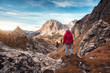 © den-belitsky - Young woman on the trail looking on high mountain peak at sunset in Dolomites, Italy. Autumn landscape with girl, path, rocks, sky with clouds at colorful sunset. Hiking in alps. Majestic mountains