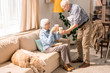 © Seventyfour - Side view portrait of adorable senior man bringing coffee to his wife in cozy living room lit by sunlight, copy space