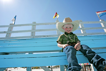 A young boy wearing a cowboy hat, sitting in the bleachers at a county fair rodeo.