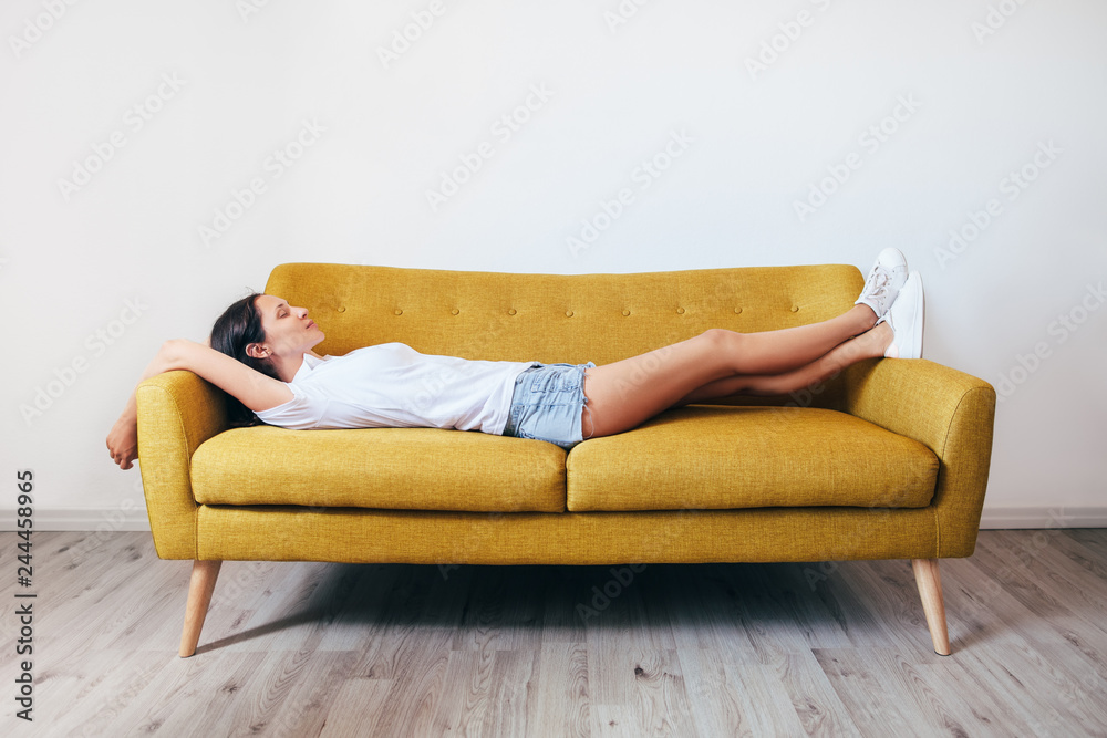 Happy young woman relaxing on couch at home - obrazy, fototapety, plakaty 