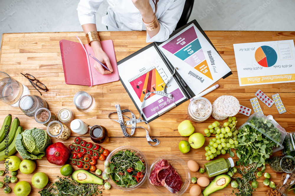 Dietitian writing diet plan, view from above on the table with different healthy products and drawings on the topic of healthy eating