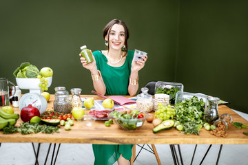 Wall Mural - Portrait of a beautiful woman as a dietitian sitting with smoothie, chia pudding and various healthy food ingredients in the green office