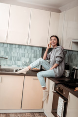 Wall Mural - Dark-haired woman wearing jeans and warm socks sitting in the kitchen