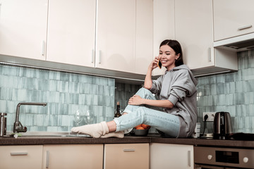Wall Mural - Dark-eyed beautiful woman speaking on the phone sitting in kitchen