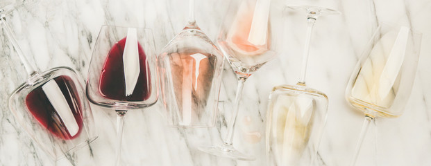 Flat-lay of red, rose and white wine in glasses and corkscrews over grey marble background, top view, wide composition. Wine bar, winery, wine degustation concept