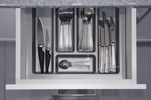 Grey opened kitchen drawer with a tray and silvery cutlery set inside. View from above. Image