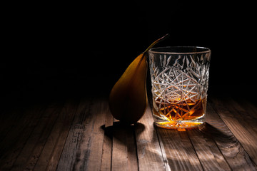 Wall Mural - Crystal glass of whiskey on a wooden table on a black background. Snack for whiskey. Cheese, almonds, pear, apple, olives, orange peel.