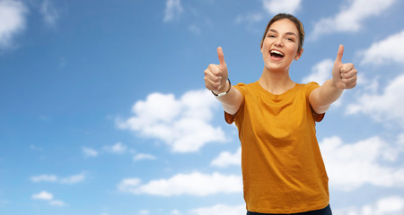 Sticker - gesture and people concept - happy smiling young woman or teenage girl in orange t-shirt showing thumbs up over blue sky and clouds background