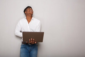 cheerful young African american man holding laptop and looking up by gray background