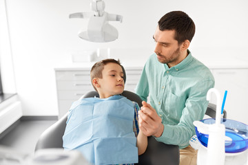 Canvas Print - medicine, dentistry and healthcare concept - father supporting son at dental clinic