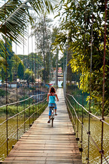 a woman riding on bicycle across suspension bridge at Si Satchanalai , Sukhothai Thailand