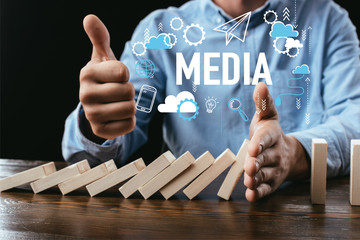 partial view of man showing thumb up sign while preventing wooden blocks from falling with word and icons on foreground