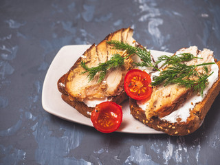 Close-up on a white plate are sandwiches of fried bread spread with cottage cheese, tomato, ham, greens, and spices on top