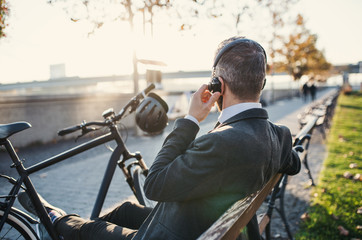 Wall Mural - Businessman commuter with bicycle sitting on bench in city, listening to music.