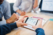 © Halfpoint - Group of businesspeople with smartphone working together in office, midsection.