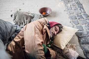 Homeless beggar man lying on the ground outdoors in city, sleeping.