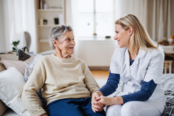 A health visitor talking to a sick senior woman sitting on bed at home.